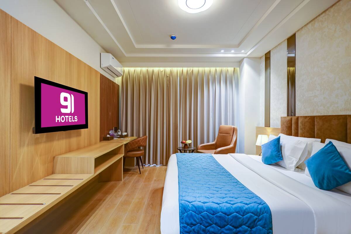 A hotel room with a bed, a desk, a chair, a TV, and a window with curtains.
