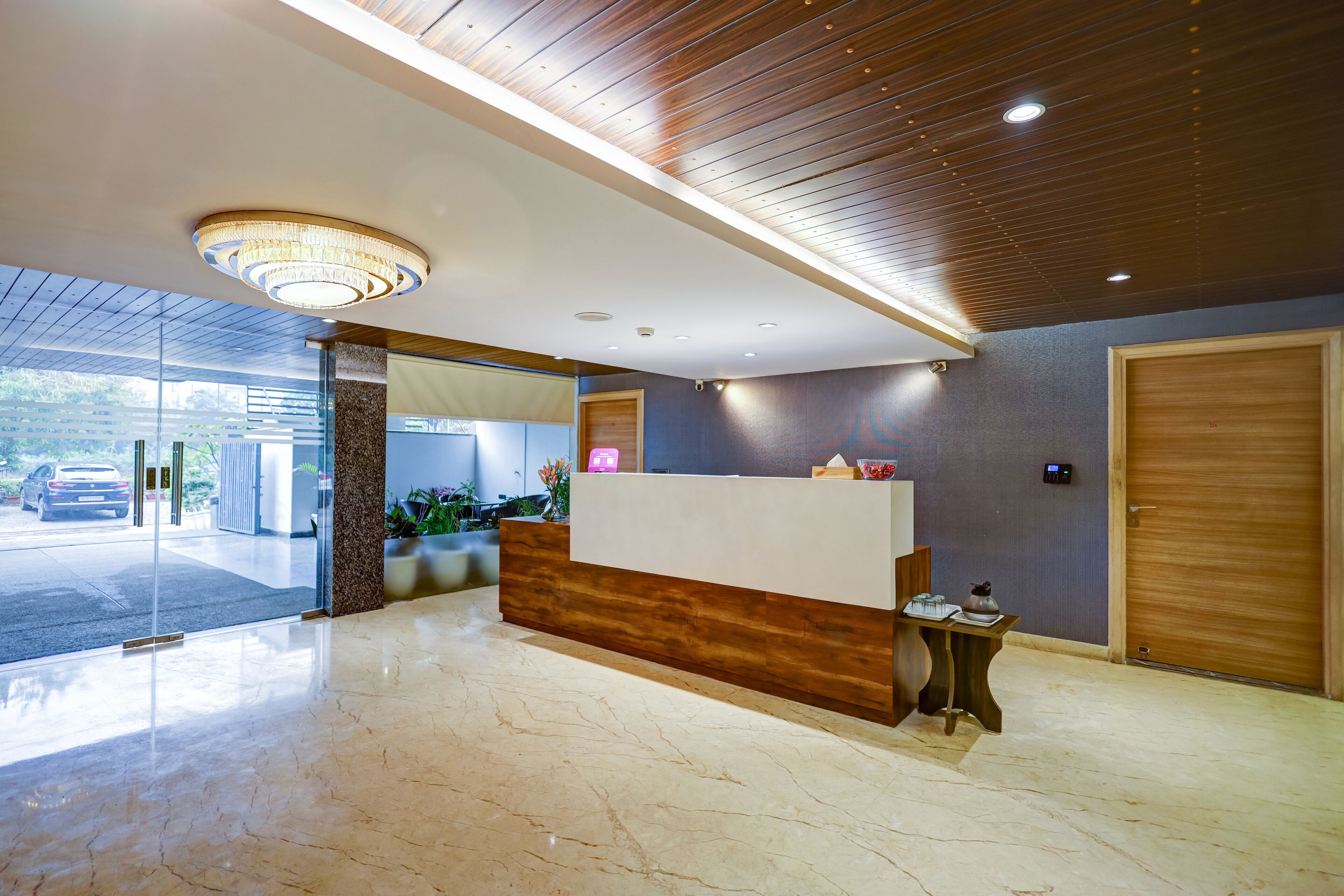 Un área de recepción con mostrador de madera, piso de mármol, candelabro y vista al estacionamiento.