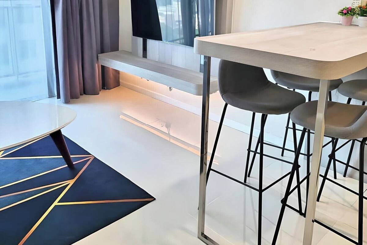 Une chambre d’hôtel moderne dotée d’un coin repas, d’une grande fenêtre avec des rideaux et d’un téléviseur à écran plat fixé au mur.