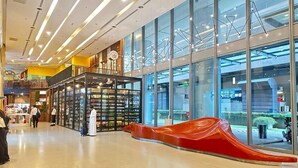 Een ruime binnenruimte met een glazen gevel, een rode glijbaan en diverse winkels en kiosken.