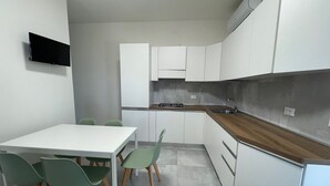 A compact kitchen with white cabinets, a wooden countertop, a built-in stove, and a TV mounted on the wall. - Renovated two-bedroom flat in Rosolina Mare (Rosolina Mare)