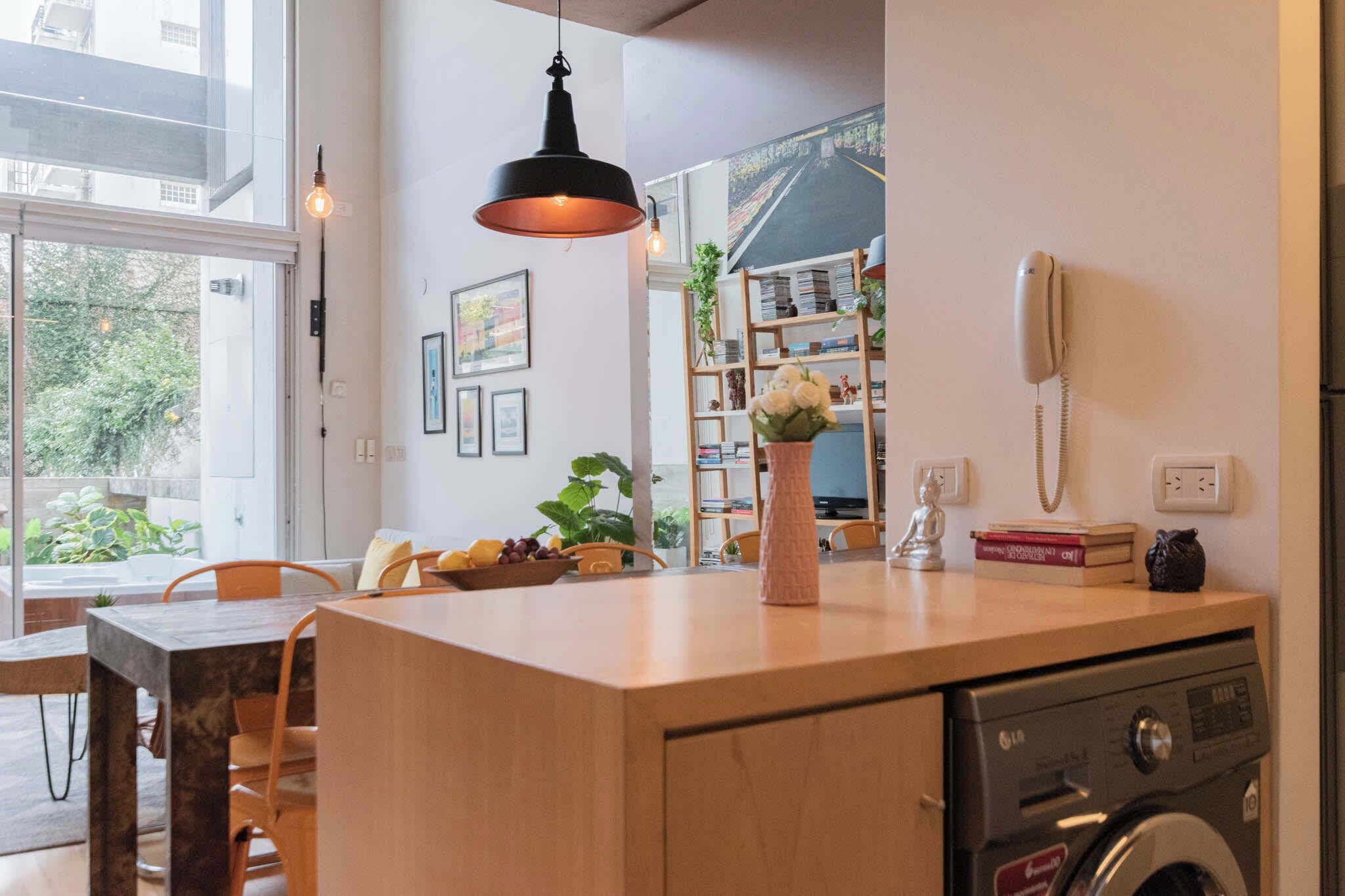 Una cocina moderna con lavadora integrada, un comedor con mesa y sillas de madera, y un amplio ventanal que ofrece vistas al exterior.