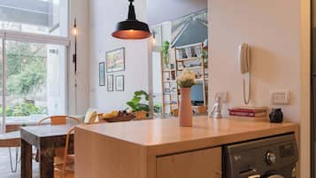 Una cocina moderna con lavadora integrada, un comedor con mesa y sillas de madera, y un amplio ventanal que ofrece vistas al exterior.