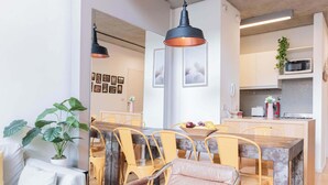 A modern dining area with a wooden table and yellow chairs, a kitchen with white cabinets, and a hanging pendant light. - MOT Rentals + Ravignani 2100 - Lux Loft Terrace & Jacuzzi (Buenos Aires)