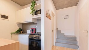 A modern kitchen with white cabinets, a stainless steel stove, and a microwave. There is a staircase leading to another level. - MOT Rentals + Ravignani 2100 - Lux Loft Terrace & Jacuzzi (Buenos Aires)
