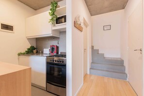 A modern kitchen with white cabinets, a stainless steel stove, and a microwave. There is a staircase leading to another level.