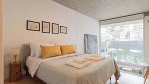 A bedroom with a bed, a nightstand, a window with a view, and framed artwork on the wall. - MOT Rentals + Ravignani 2100 - Lux Loft Terrace & Jacuzzi (Buenos Aires)