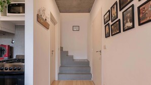 A narrow hallway with a staircase leading to a landing. There is a kitchen area on the left with a stove and a microwave. The walls are decorated with framed pictures. - MOT Rentals + Ravignani 2100 - Lux Loft Terrace & Jacuzzi (Buenos Aires)