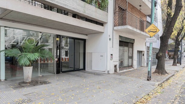 A modern building with a glass entrance, a potted plant, and a yellow caution sign. - MOT Rentals + Ravignani 2100 - Lux Loft Terrace & Jacuzzi (Buenos Aires)