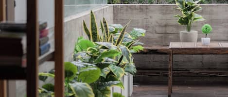Une terrasse en bois agrémentée de plantes en pot, un mur en béton et une petite table.