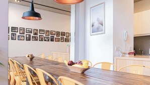 A dining area with a long wooden table, yellow chairs, and a fruit bowl. There are framed pictures on the wall and a kitchen area with a phone and a tiled backsplash. - MOT Rentals + Ravignani 2100 - Lux Loft Terrace & Jacuzzi (Buenos Aires)