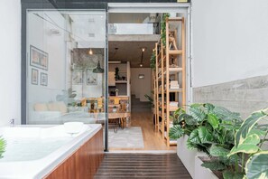 Un interior moderno con una puerta de cristal que da a una sala de estar, una escalera de madera y una planta grande.