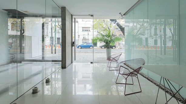 A modern interior with a glass wall, a seating area with wireframe chairs, and a view of the street outside. - MOT Rentals + Ravignani 2100 - Lux Loft Terrace & Jacuzzi (Buenos Aires)