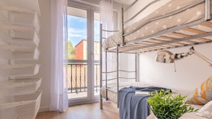 Et kollegieværelse med køjesenge, en balkon, et skrivebord med lampe og en potteplante.