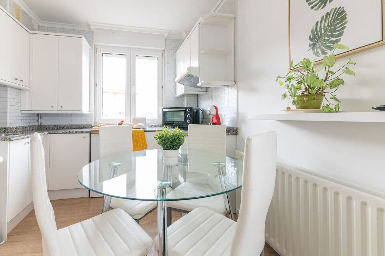 Een moderne keuken met witte kastjes, een glazen eettafel en een potplant.