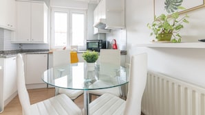 Et moderne køkken med hvide skabe, et glasbord og en potteplante.