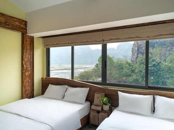 Habitación de hotel con dos camas, un ventanal con vistas a un río y montañas, y cabecero de madera.