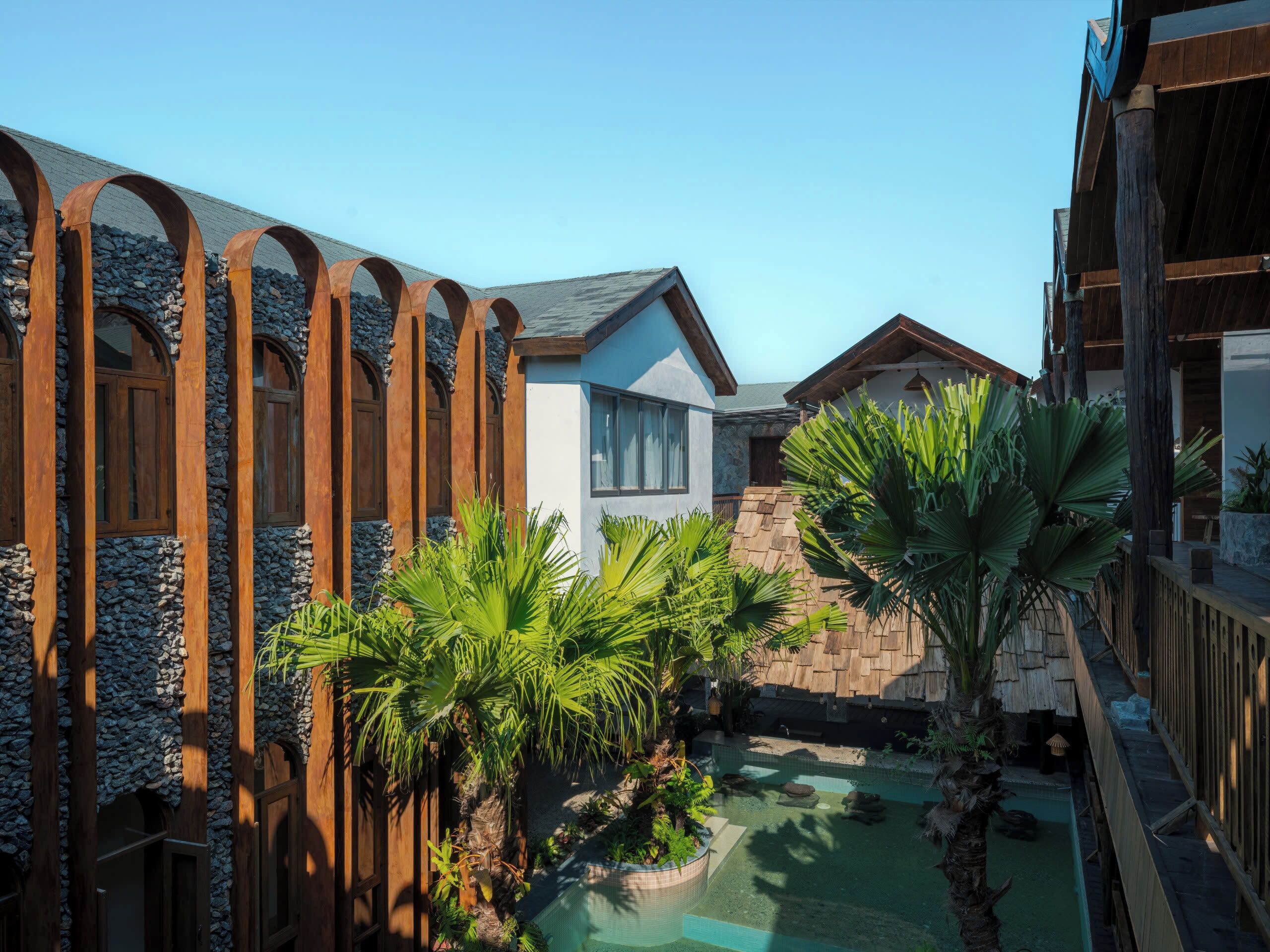 A resort with a pool, wooden pergolas, and tropical plants.