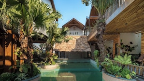 A pool area with a stone wall, palm trees, and a wooden deck. - AiLee Villa & Hotel Tamcoc (Nam Hoa Lu)
