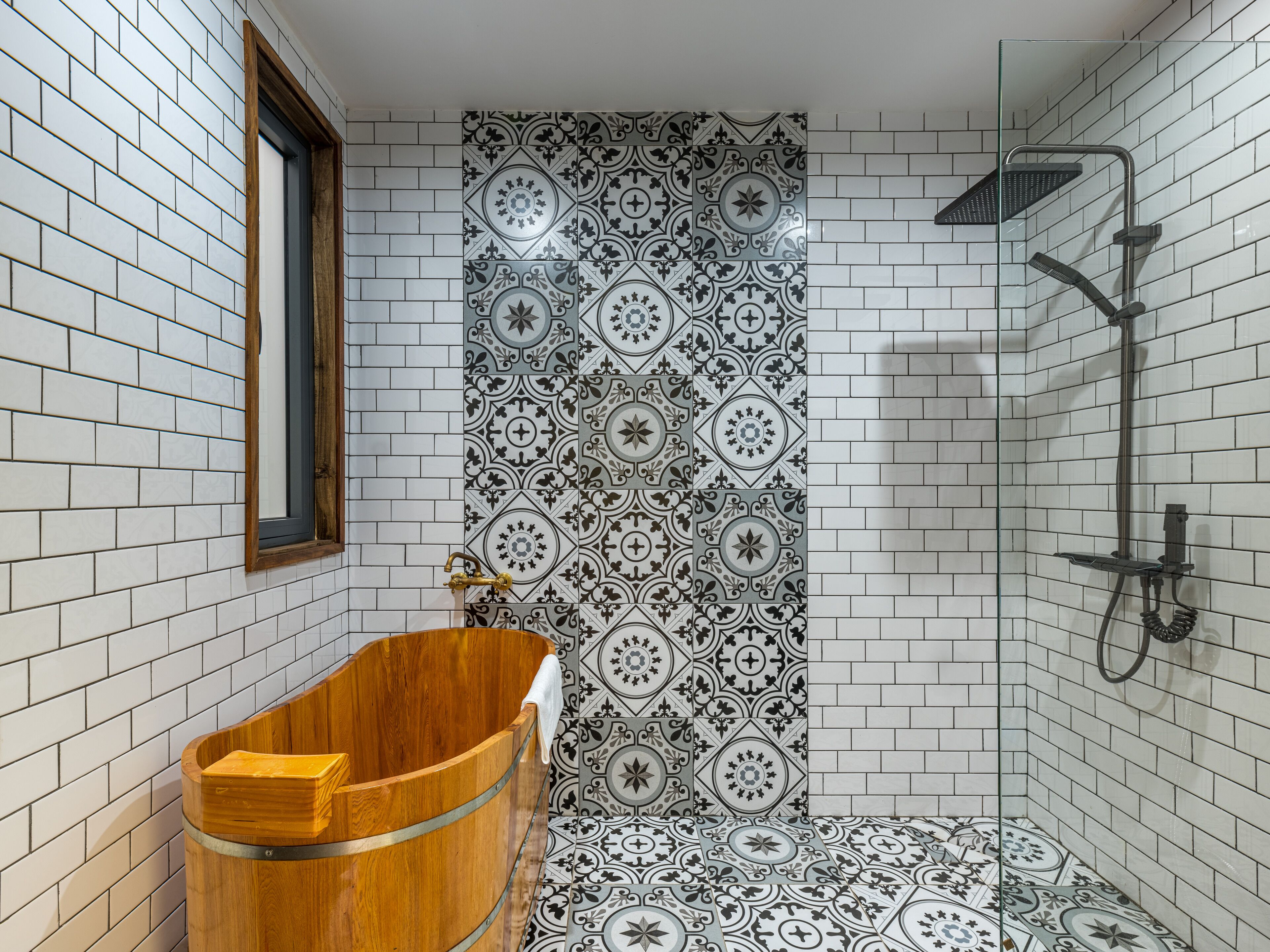 A bathroom with a wooden bathtub, a shower, and patterned tiles.