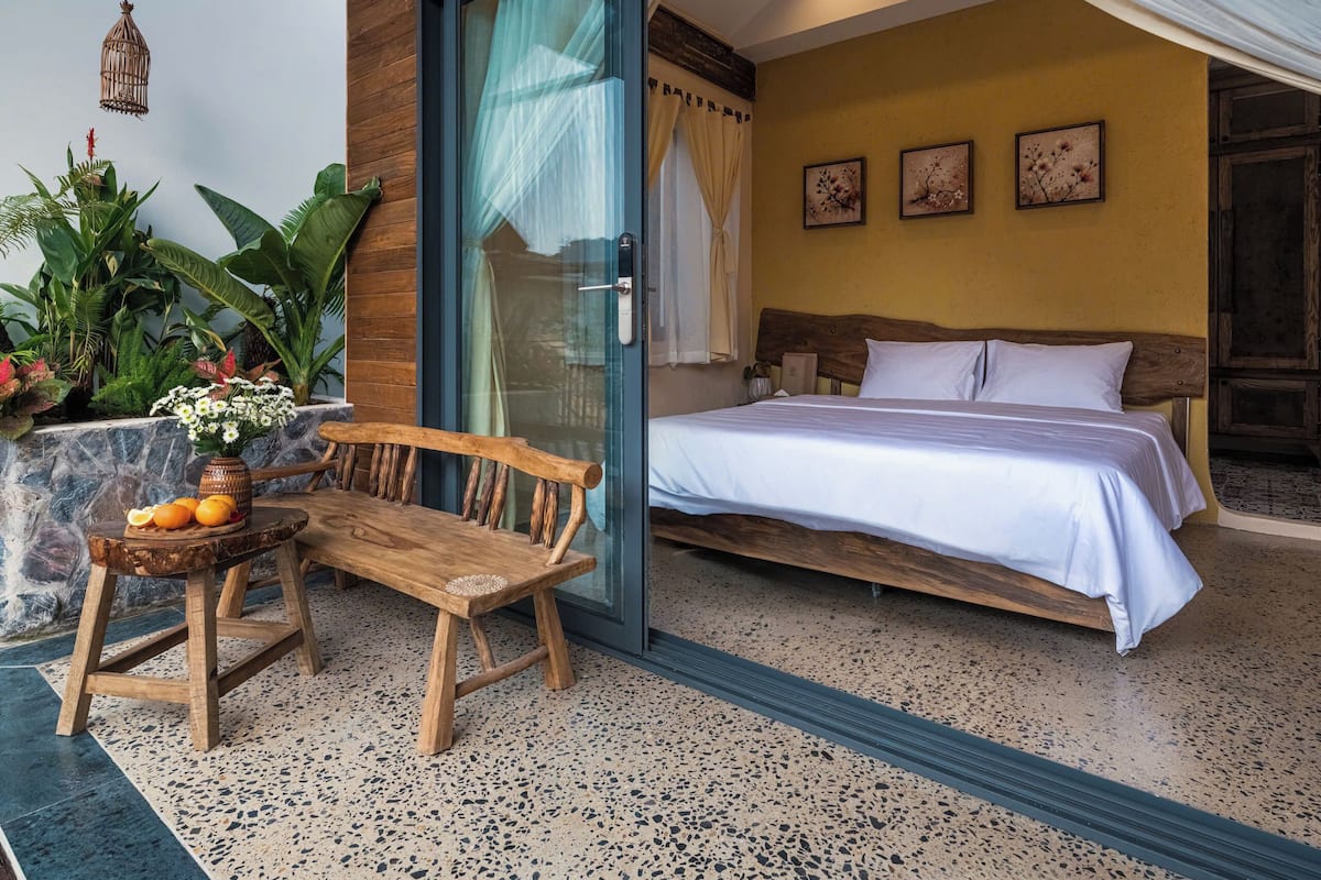 A bedroom with a bed, a wooden bench, a small table with fruit, and a vase of flowers.