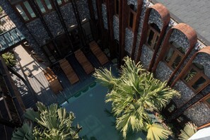 Un área de piscina en la azotea con tumbonas de madera, palmeras y un muro de piedra.