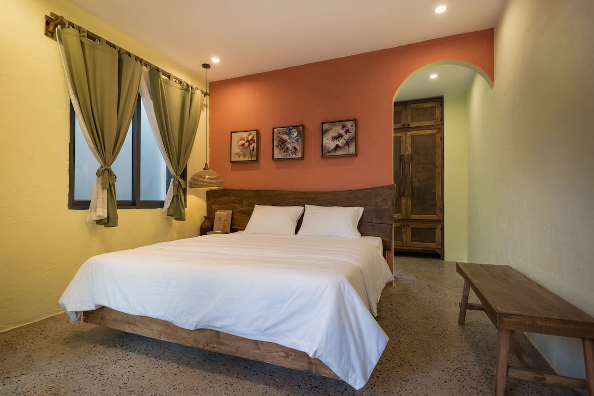 A bedroom with a wooden bed, green curtains, and a bench.