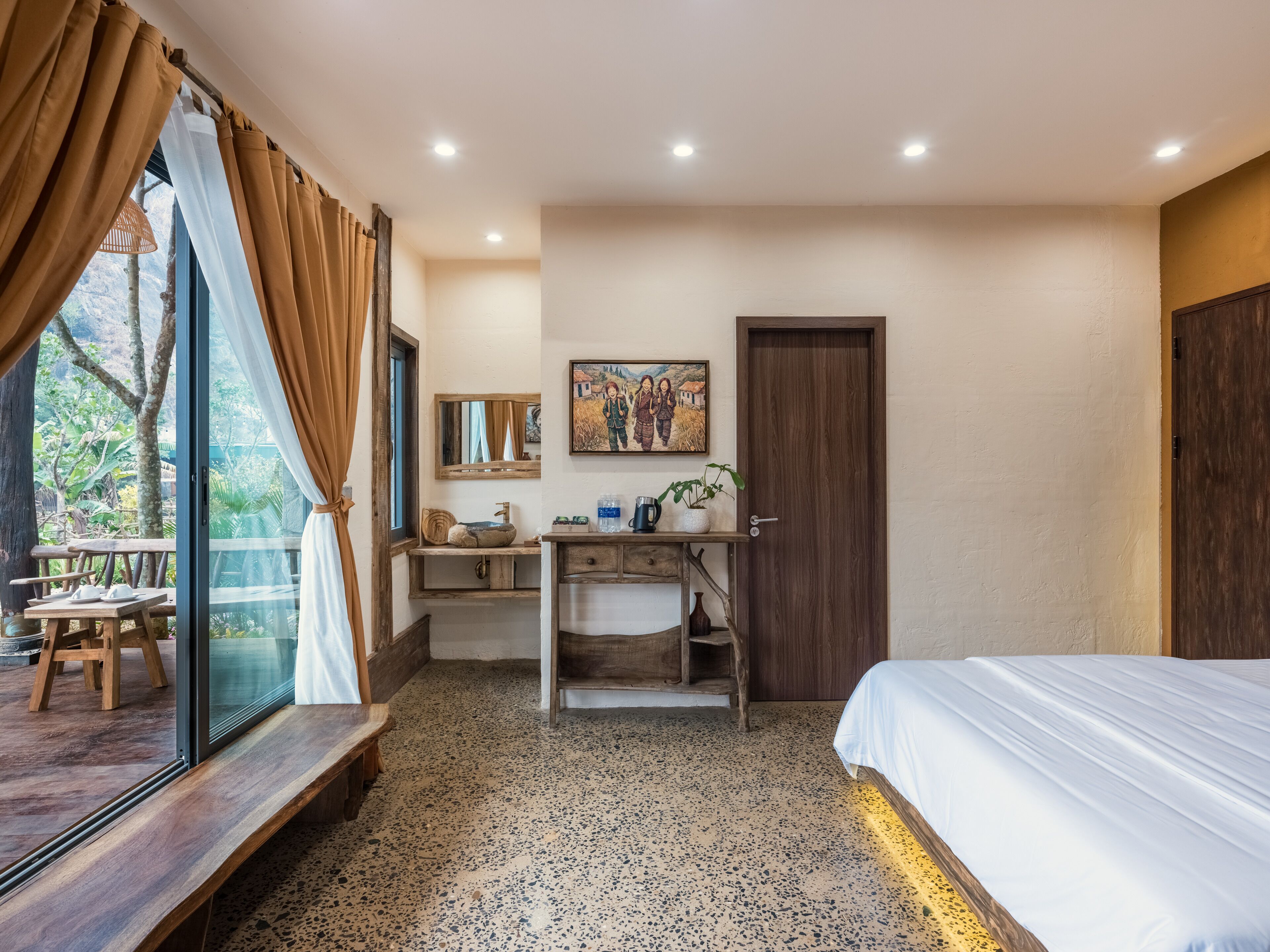 A bedroom with a bed, a wooden bench, a sink, and a window with curtains.