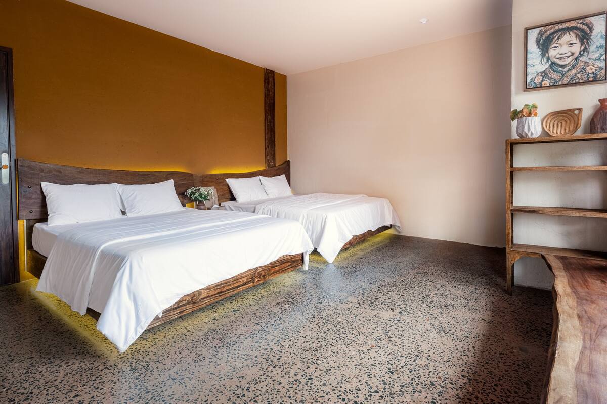 A hotel room with two beds, a wooden headboard, a speckled floor, and a shelf with decorative items.