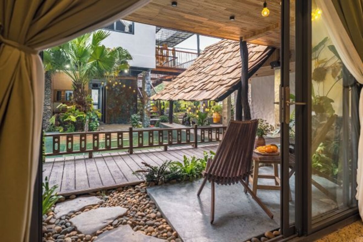 Une terrasse en bois avec une chaise, une table garnie de fruits et une vue sur un jardin avec des plantes et une piscine.