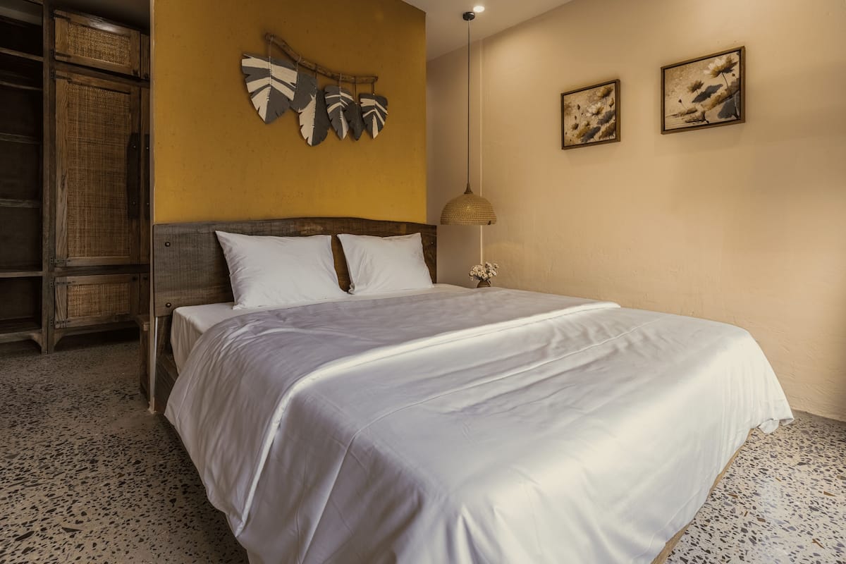 A bedroom with a large bed, a wooden headboard, a wall-mounted artwork, and a textured floor.