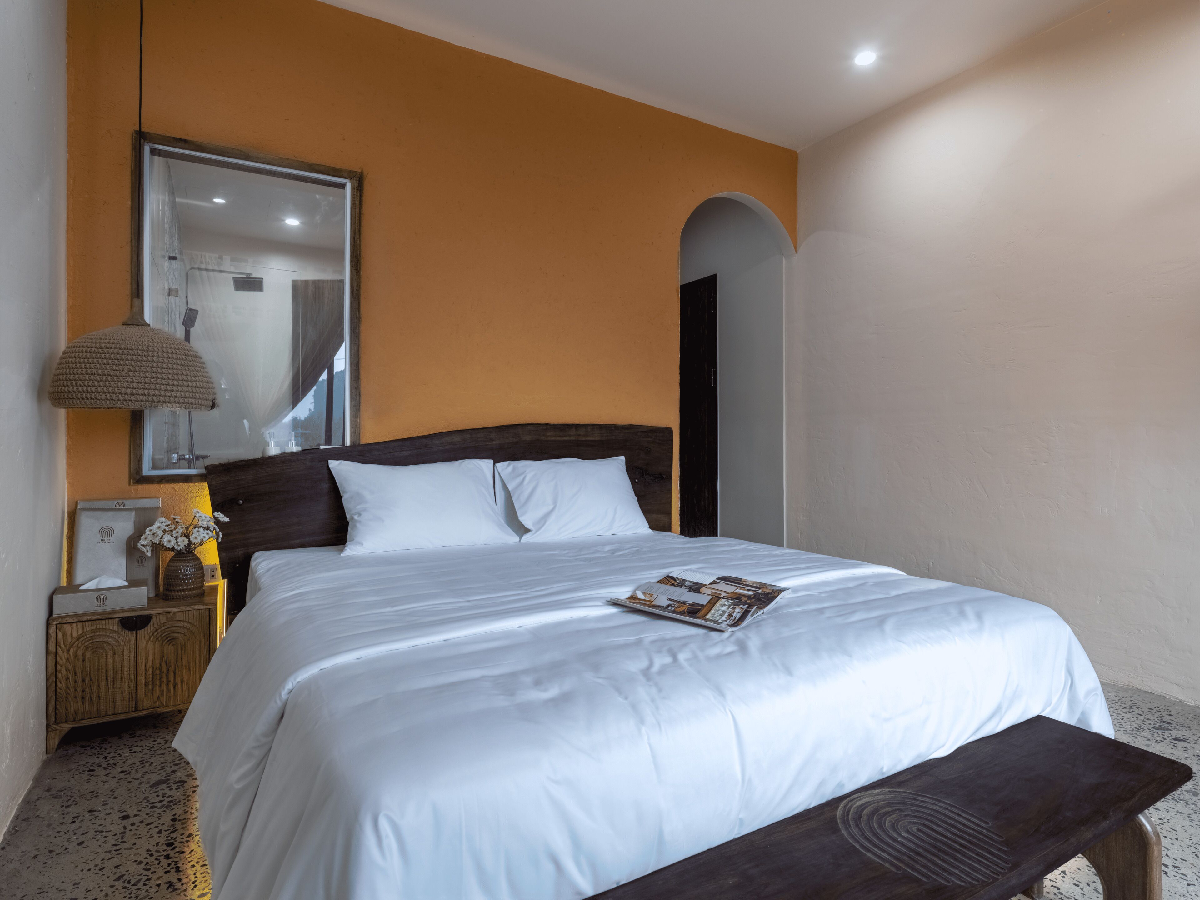 Una cama bien hecha con ropa blanca, un cabecero de madera, una lámpara de noche y una revista sobre la cama.