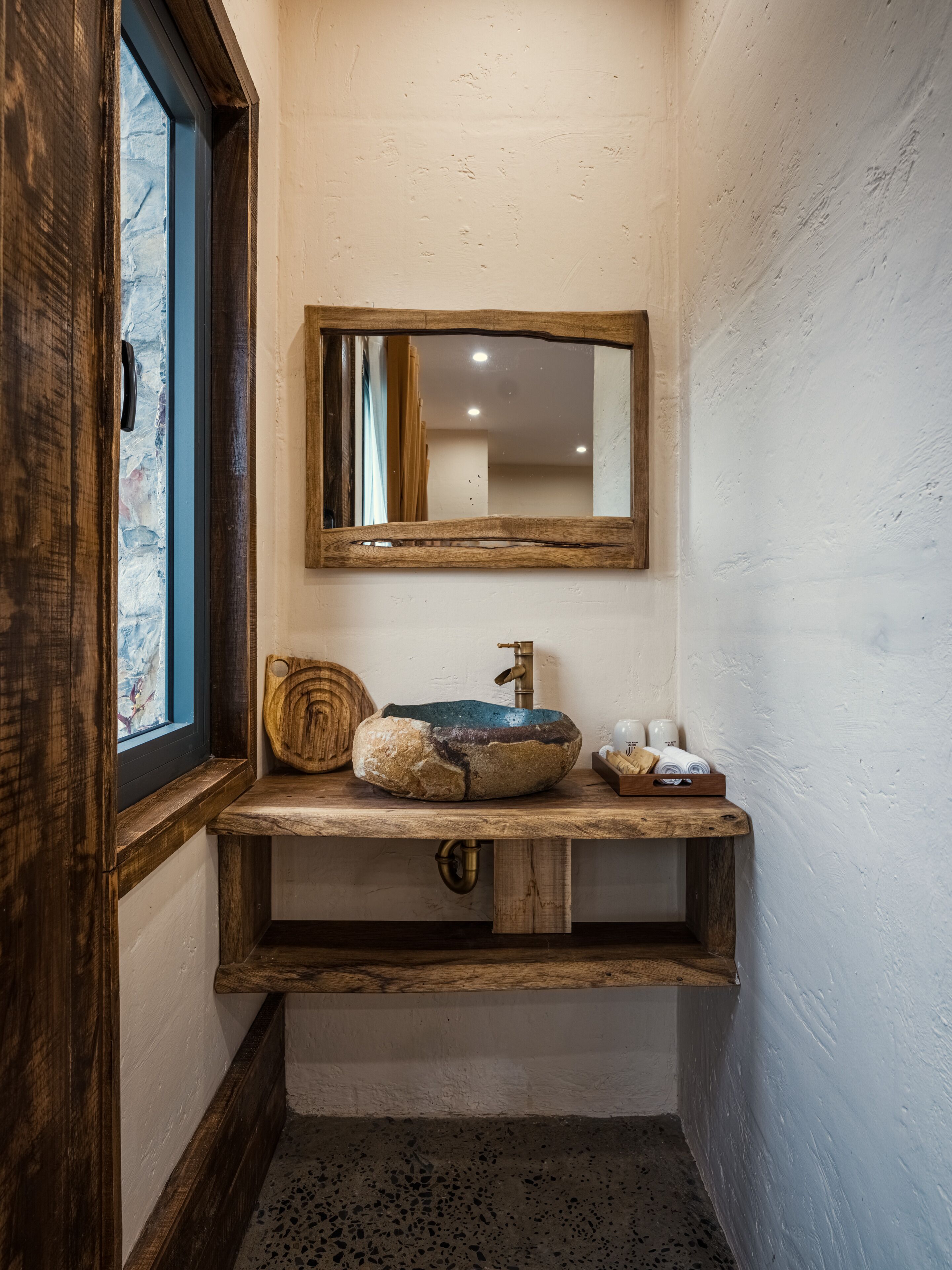 A rustic bathroom with a wooden vanity, a stone sink, and a mirror.