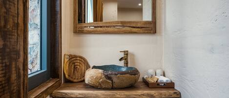A rustic bathroom with a wooden vanity, a stone sink, and a mirror.
