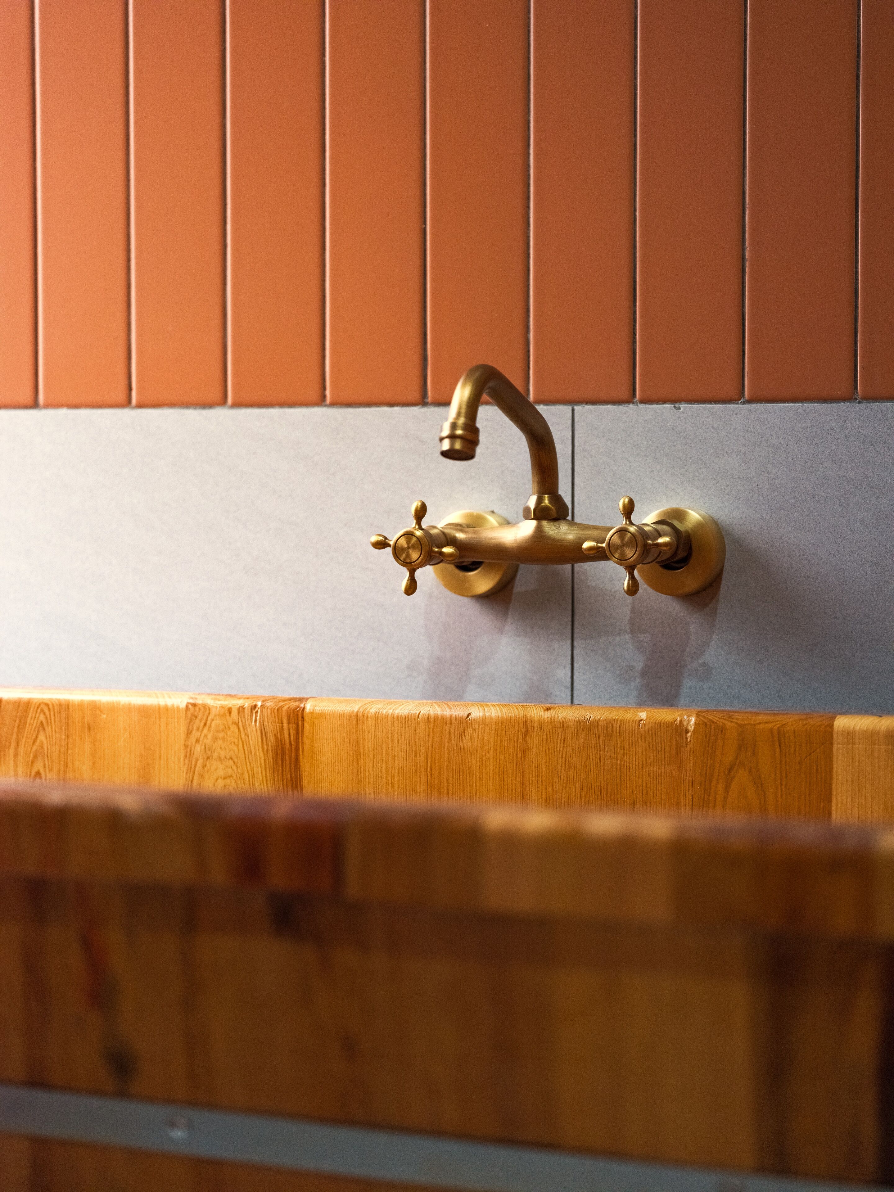 Ein Badezimmer mit einem messingfarbenen Wasserhahn an einer gefliesten Wand.