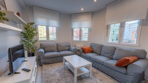 Uma sala de estar moderna com sofás cinzas, uma mesa de centro branca e uma TV sobre um suporte branco.
