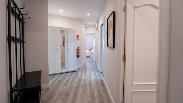 Um corredor com piso de madeira, paredes brancas e uma porta à direita.