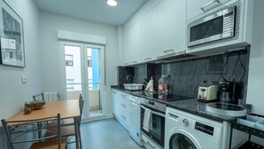 Uma cozinha moderna com armários brancos, micro-ondas, torradeira e máquina de lavar.
