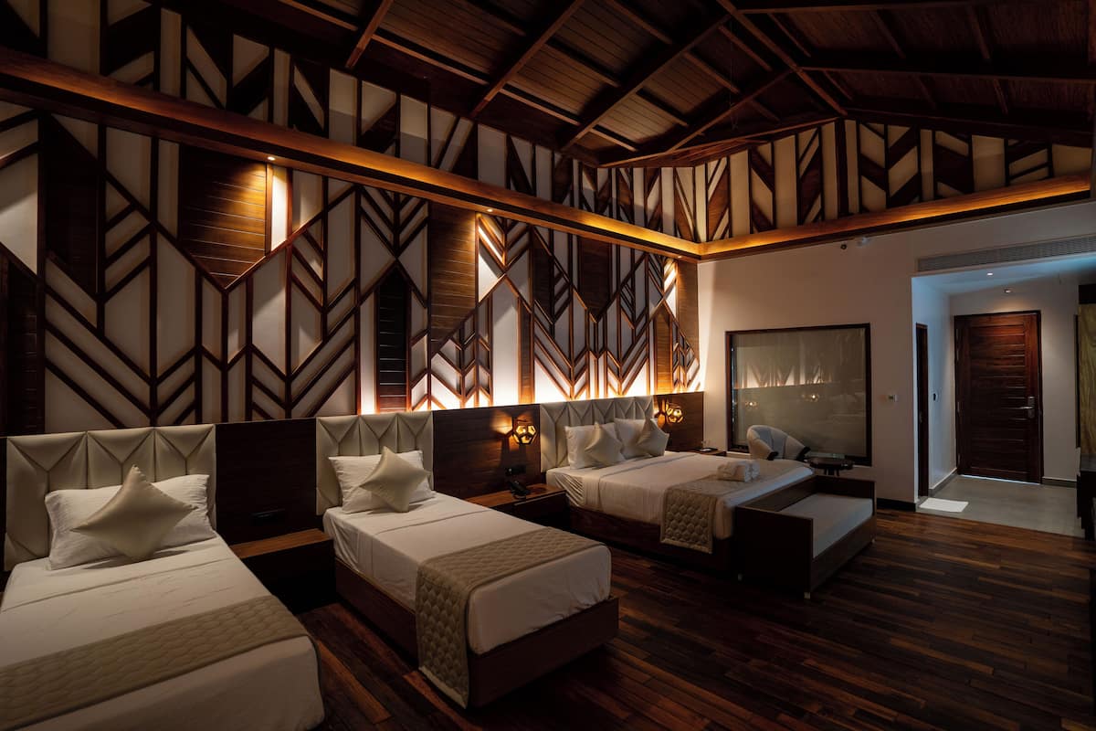 A hotel room with three beds, wooden flooring, and a geometric patterned wall.