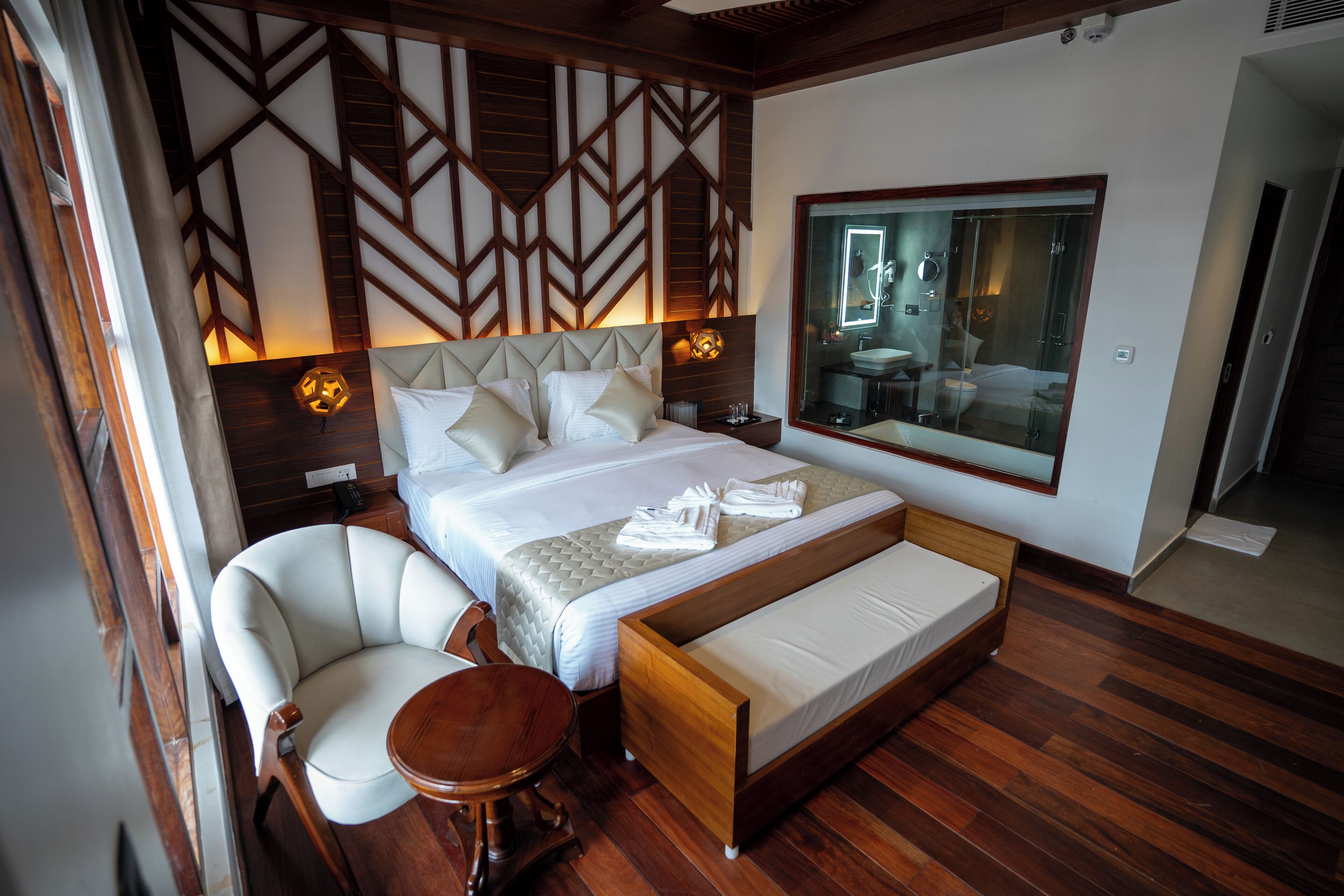 A bedroom with a large bed, a chair, a small table, and a large mirror.