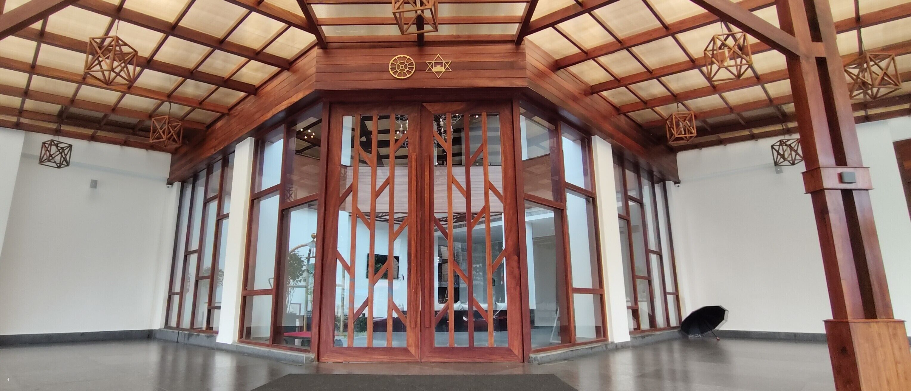 A spacious lobby with a high ceiling and wooden beams, large glass doors, and geometric hanging lights.