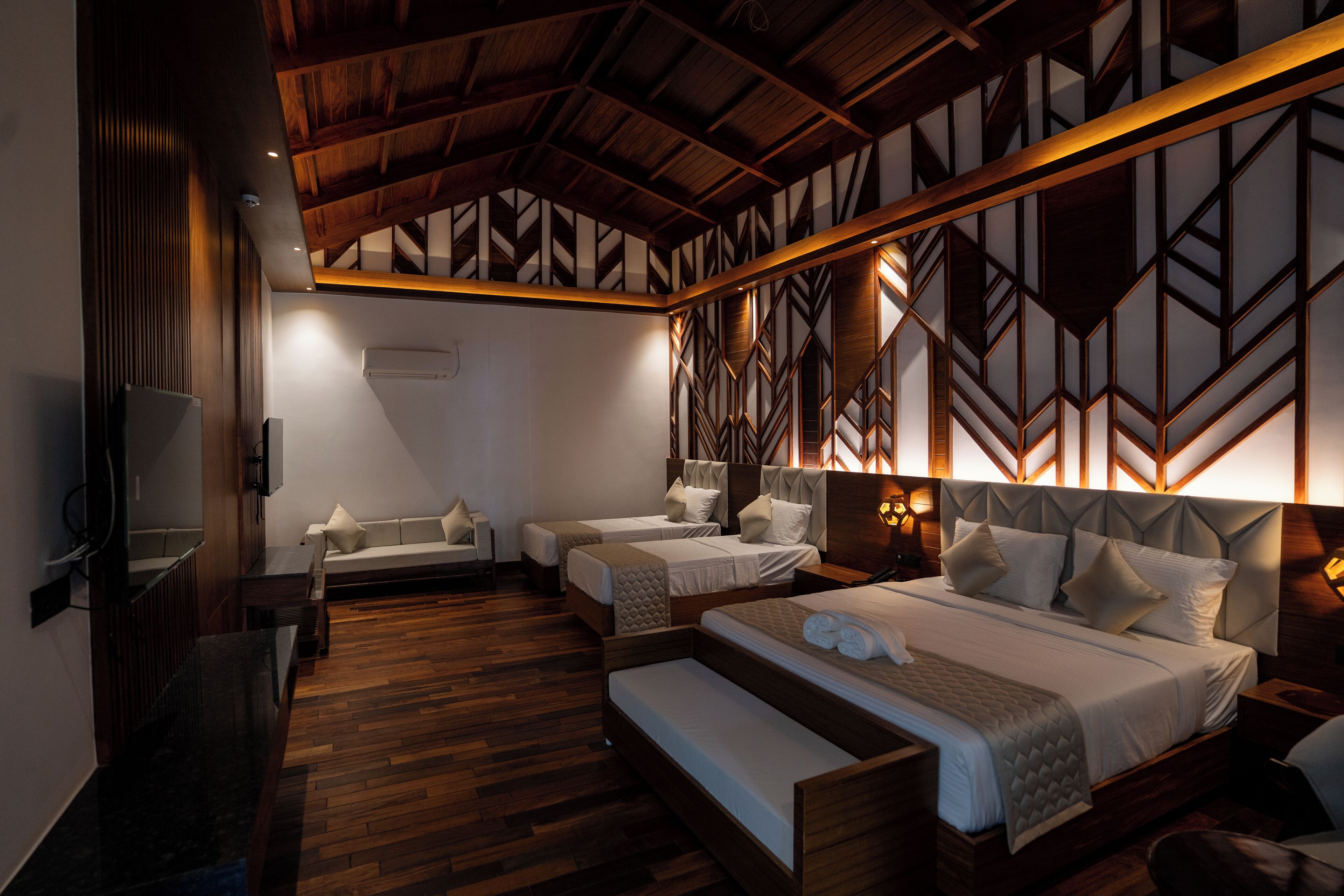 A hotel room with a wooden ceiling, two beds, a sofa, and a TV.