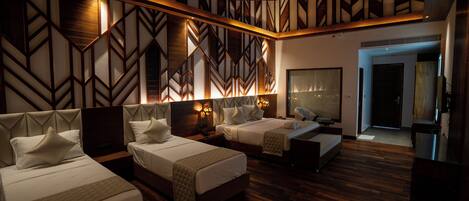 A hotel room with three beds, wooden flooring, and a geometric-patterned wall.