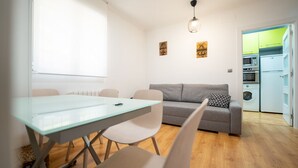 A modern living room with a grey sofa, a glass dining table, and a kitchen area visible through an open door. - Apto tranquilo y luminoso con cocina equipada (Santander)