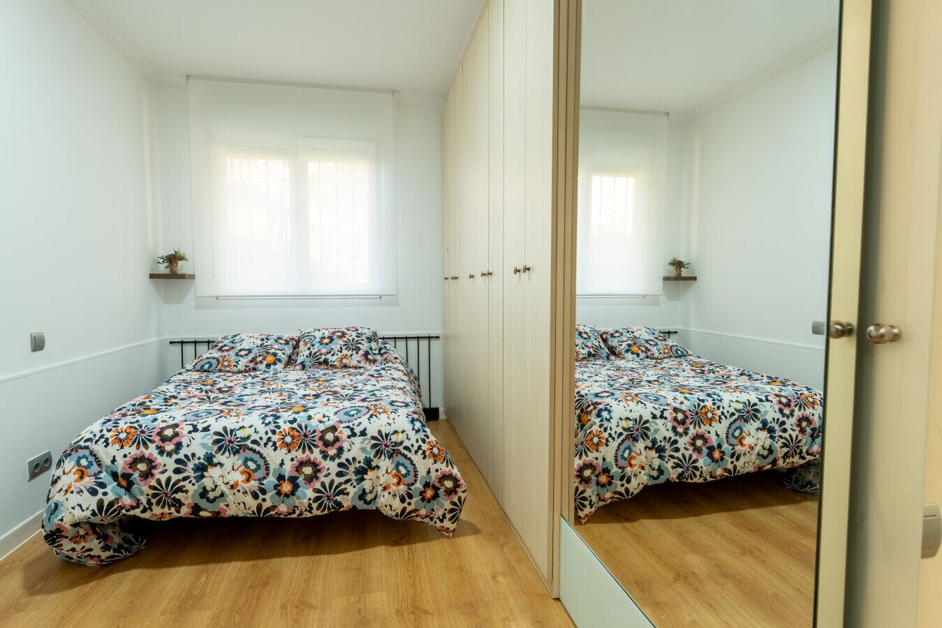 Een slaapkamer met twee bedden, een grote spiegel en een raam met zonwering.