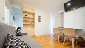 A modern living room with a grey sofa, two beige chairs, a wooden dining table, and a TV mounted on the wall. - Apto tranquilo y luminoso con cocina equipada (Santander)