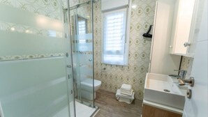 Et badeværelse med brusekabine i glas, toilet, vask og et vindue.