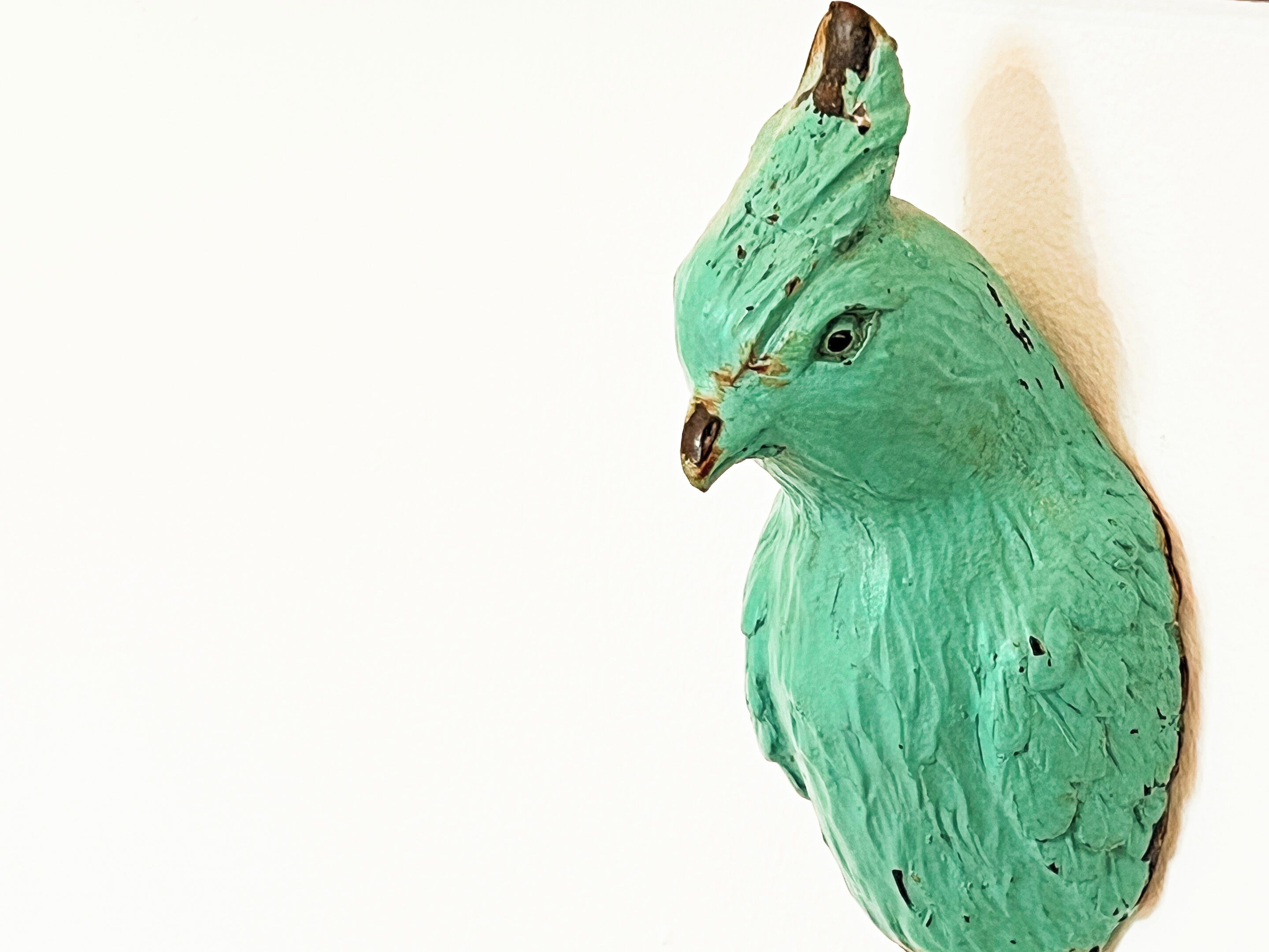 A green bird sculpture on a white wall.