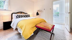 Ein Schlafzimmer mit einem Bett, einem Nachttisch, einer Lampe, einer Hängelampe, einem Fenster mit Jalousien und einer Tür, die auf einen Balkon führt.