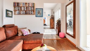 Una sala de estar con un sofá de cuero marrón, una mesa de centro con un jarrón, una estantería llena de libros y un ventanal con vista a la calle.